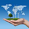 Wind turbines on meadow with tree holds in womans hand against blue sky and map of the world made of clouds. Worldwide Green energy concept
