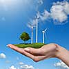 Wind turbines on meadow with tree holds in womans hand against blue sky and clouds. Green energy concept