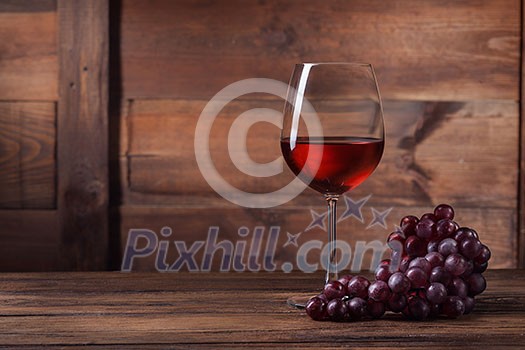 Red wine in glass with grape on wooden background