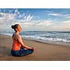 Young sporty fit woman doing yoga - meditating and relaxing in Padmasana Lotus Pose) with chin mudra outdoors at tropical beach on sunset