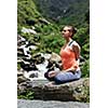 Young sporty fit woman doing yoga - meditating in Baddha Padmasana (Bound Lotus Pose) outdoors at tropical waterfall