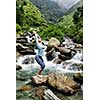 Young sporty fit woman doing yoga asana Utkatasana (chair pose) outdoors at tropical waterfall standing on stone