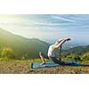 Sporty fit woman practices yoga Anjaneyasana - low crescent lunge pose outdoors in mountains in morning
