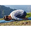 Sporty fit woman practices yoga asana Balasana - child pose outdoors in mountains