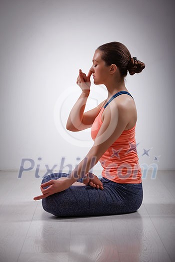 Beautiful sporty fit yogini woman practices pranayama breath control exercise in yoga asana Padmasana - lotus pose with Vishnu mudra in studio Beautiful sporty fit yogini woman practices pranayama breath control exercise in yoga asana Padmasana - lotus pose with Vishnu mudra in studio