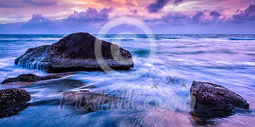 Tropical beach vacation background - panorama of waves and rocks on beach on sunset with beautiful cloudscape