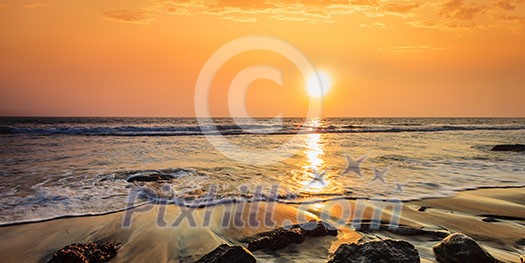 Tropical beach vacation background - panorama of waves and rocks on beach on sunset with beautiful cloudscape Tropical beach vacation background - panorama of waves and rocks on beach on sunset with beautiful cloudscape