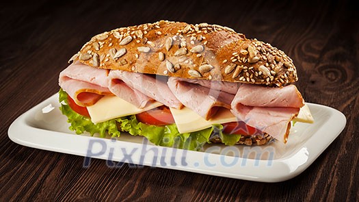 Panorama of ham sandwich with lettuce, cheese, tomato on plate on wooden table Panorama of ham sandwich with lettuce, cheese, tomato on plate on wooden table