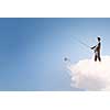 Young businessman standing on cloud high in sky and fishing
