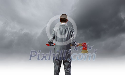 Rear view of young determined businessman with axe in hands
