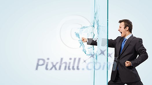 Young determined businessman breaking glass with karate punch