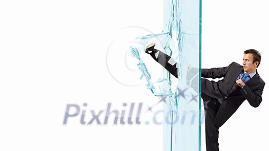 Young determined businessman breaking glass with karate kick