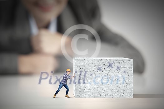 Businesswoman looking at miniature of builder pushing wall Businesswoman looking at miniature of builder pushing wall