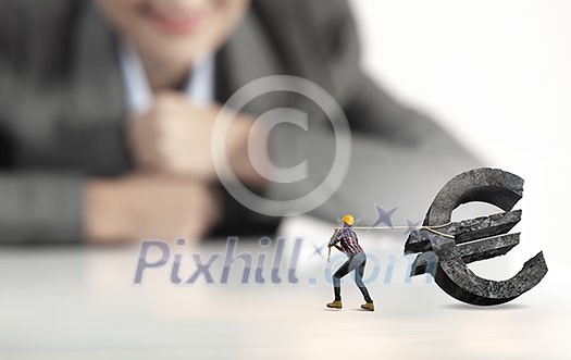 Businesswoman looking at miniature of builder pulling euro sign Businesswoman looking at miniature of builder pulling euro sign