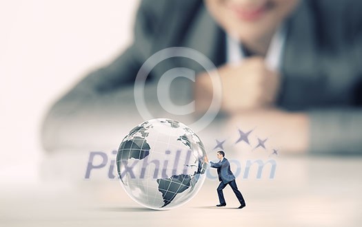 Businesswoman looking at miniature of businessman rolling planet Businesswoman looking at miniature of businessman rolling planet