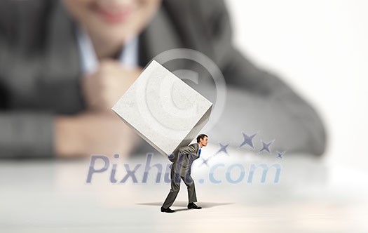 Businesswoman looking at miniature of man carrying white cube on back Businesswoman looking at miniature of man carrying white cube on back