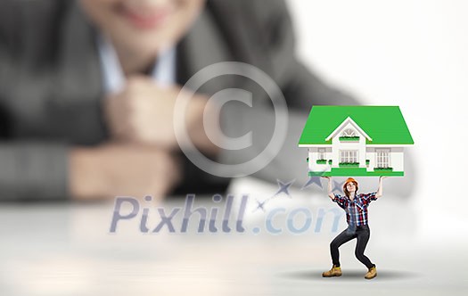Businesswoman looking at miniature of woman builder holding model house Businesswoman looking at miniature of woman builder holding model house