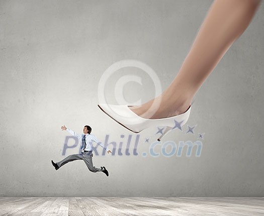 Businesswoman foot stepping on tiny businessman presenting power concept Businesswoman foot stepping on tiny businessman presenting power concept