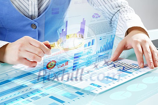 Close up of business person investigating infographs with magnifier Close up of business person investigating infographs with magnifier