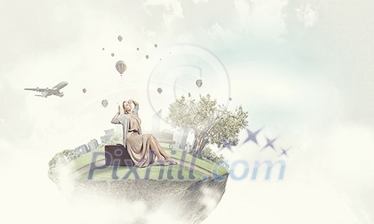 Woman in long dress and hat sitting on retro suitcase Woman in long dress and hat sitting on retro suitcase