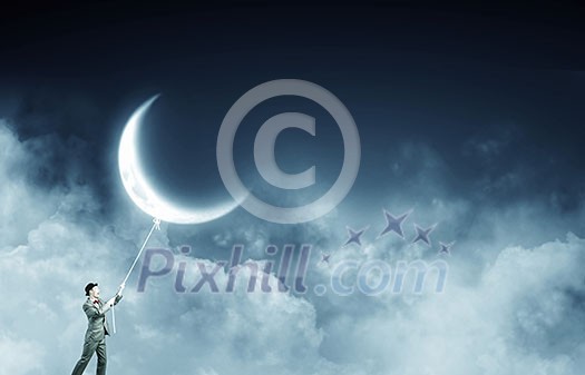 Young businessman in hat who obtains moon with rope Young businessman in hat who obtains moon with rope