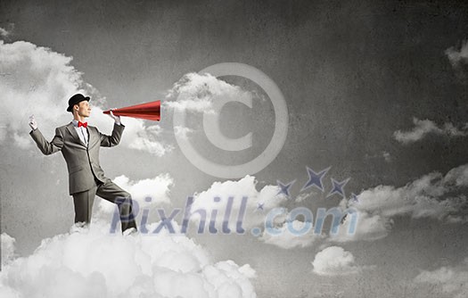 Young businessman on cloud screaming emotionally in paper trumpet Young businessman on cloud screaming emotionally in paper trumpet