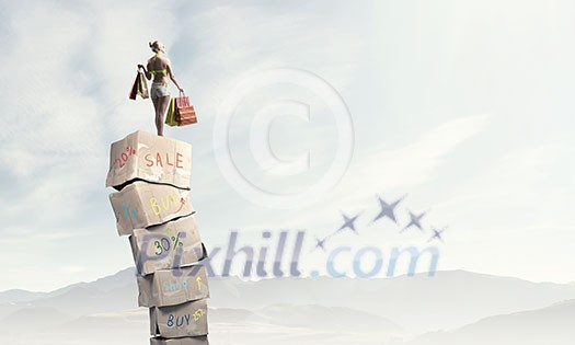 Beautiful young girl in bikini with shopping bags on pile of carton boxes Beautiful young girl in bikini with shopping bags on pile of carton boxes