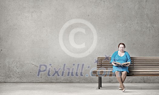 Plus size woman with book in hands sitting on bench