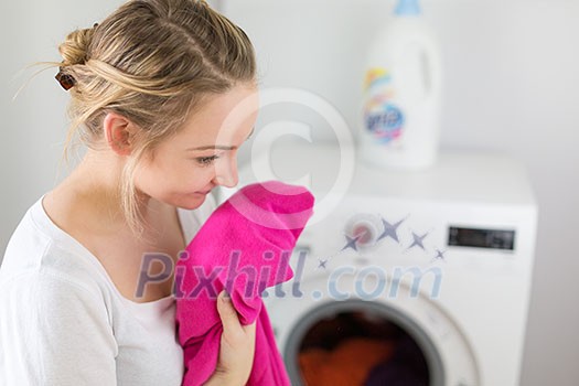 Housework: young woman doing laundry - putting colorful garments into the washing machine (shallow DOF; color toned image)