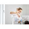Housework: young woman doing laundry - putting colorful garments into the washing machine (shallow DOF; color toned image)
