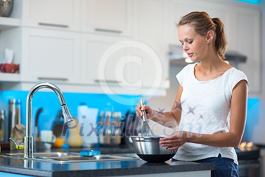 Pretty, young woman in her modern, clean and bright kitchen, fixing lunch/cooking/baking (color toned imagey; shallow DOF)