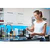 Pretty, young woman in her modern, clean and bright kitchen, fixing lunch/cooking/baking (color toned imagey; shallow DOF)