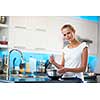 Pretty, young woman in her modern, clean and bright kitchen, fixing lunch/cooking/baking/making pancakes (color toned imagey; shallow DOF)