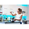 Pretty, young woman in her modern, clean and bright kitchen, fixing lunch/cooking/baking/making pancakes (color toned imagey; shallow DOF)