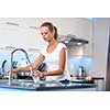 Pretty, young woman in her modern, clean and bright kitchen, pouring herself and drinking a glass of cold tap water(color toned imagey; shallow DOF)