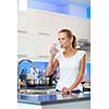 Pretty, young woman in her modern, clean and bright kitchen, pouring herself and drinking a glass of cold tap water(color toned imagey; shallow DOF)