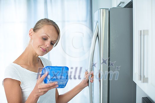 Is this still fine? Pretty, young woman in her kitchen by the fridge, looking at the expiry date of a product she took from her fridge -