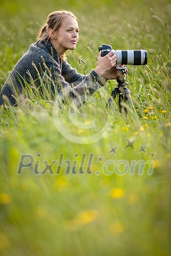 Pretty young woman with a DSLR camera outdoors, using a tripod, taking pictures