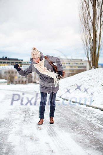 Pretty, young woman having troubles walking on an icy, slippery sidewalk after a snowfall during the big freeze period (color toned image; shallow DOF)