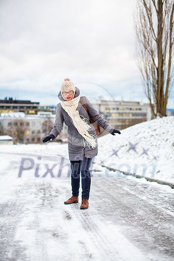 Pretty, young woman having troubles walking on an icy, slippery sidewalk after a snowfall during the big freeze period (color toned image; shallow DOF)