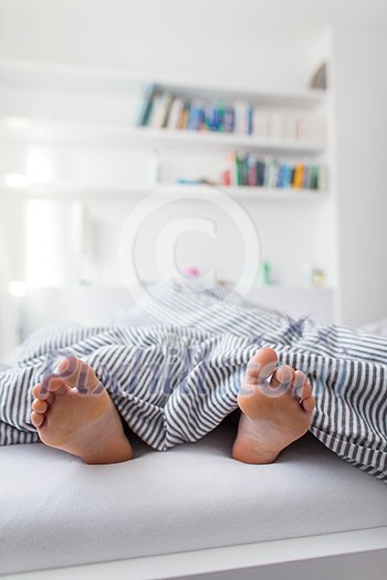 Feet of a person sleeping in bed in bright, sunlit modern bedroom (shalow DOF; color toned image)