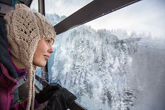 Pretty, young woman admiring splendid winter scenery from a cablecar cabin in high mountains (shallow DOF; color toned image)