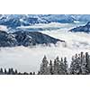 Splendid winter alpine scenery with high mountains and trees covered with snow, clouds hanging low in the valley