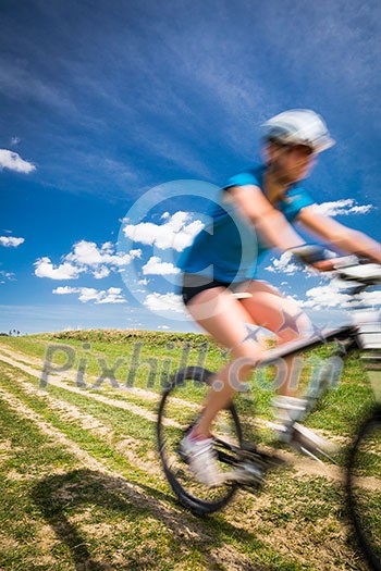 Pretty, young female biker outdoors on her mountain bike (motion blurred image)