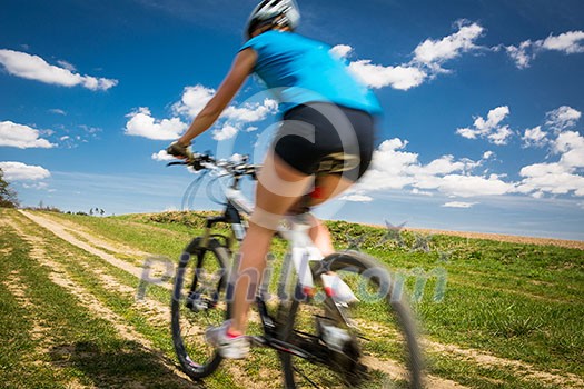 Pretty, young female biker outdoors on her mountain bike (motion blurred image)