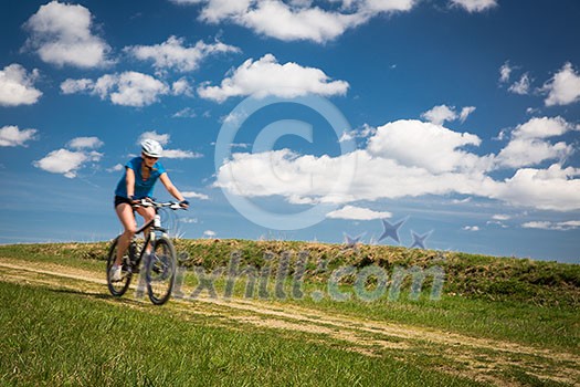 Pretty, young female biker outdoors on her mountain bike (motion blurred image)