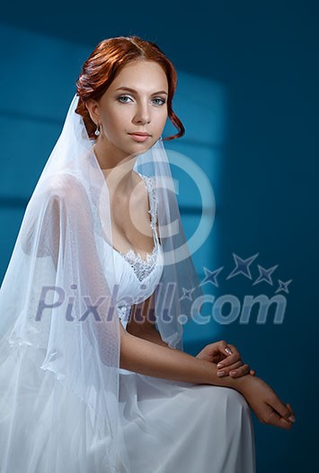 Beautiful bride on a blue background. Wedding dress, veil, red hair.