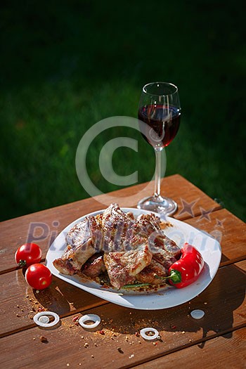 Grilled pork steaks on a wooden table with a glass of wine at sunset