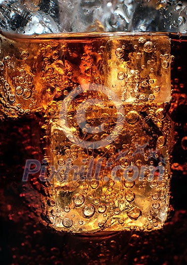 Bubbles in the glass of cola with ice. Close-up.