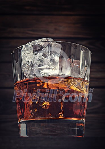 Glass of whiskey with ice on a wooden background made with vintage tones. Toned like instagram. Glass of whiskey with ice on a wooden background made with vintage tones. Toned like instagram.